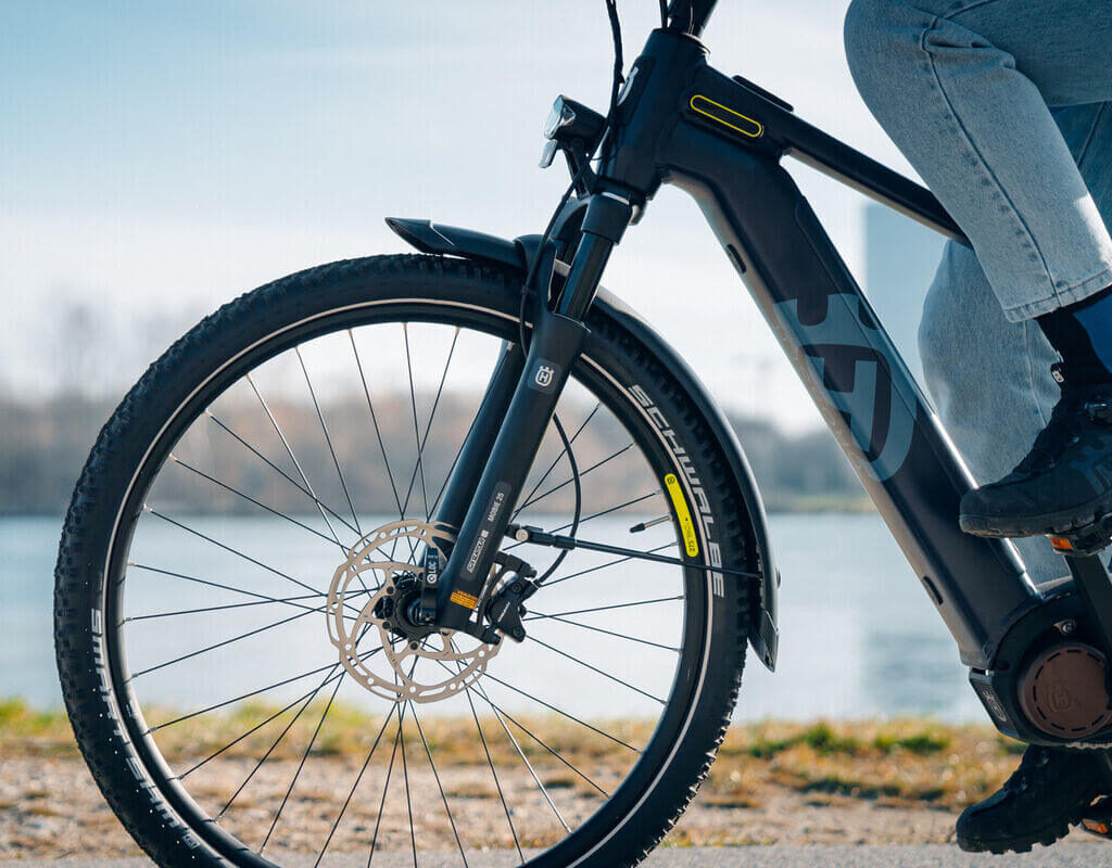 Detailed view of an electric bicycle with focus on the front wheel and fork, ridden by one person.