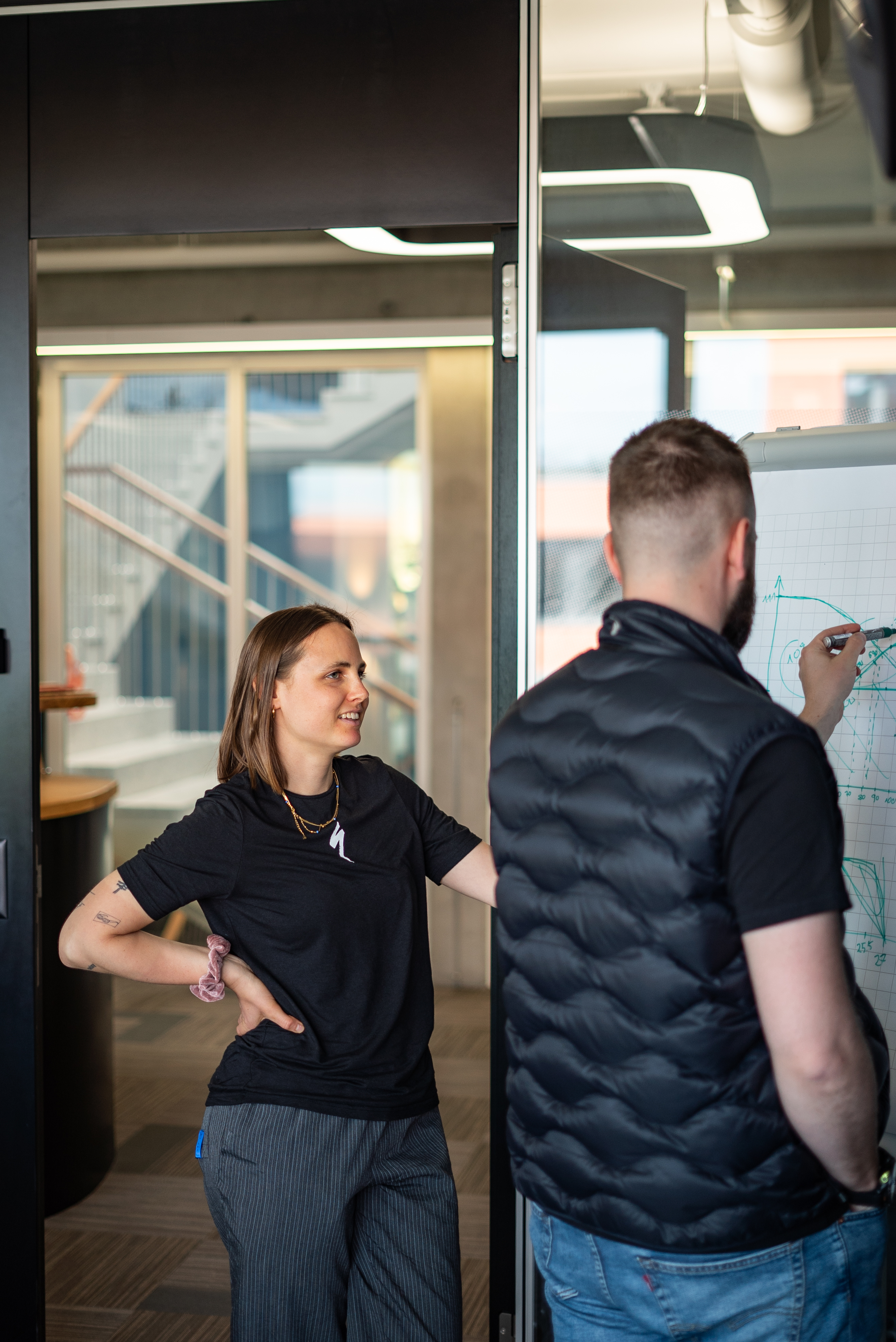 Sofia and a second person are standing in front of a flipchart with graphic sketches, one of whom is actively writing. 