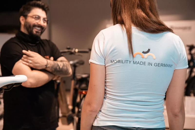 Ein Mann und eine Frau stehen sich gegenüber, die Frau trägt ein T-Shirt mit der Aufschrift „Mobility Made in Germany“ auf dem Rücken.