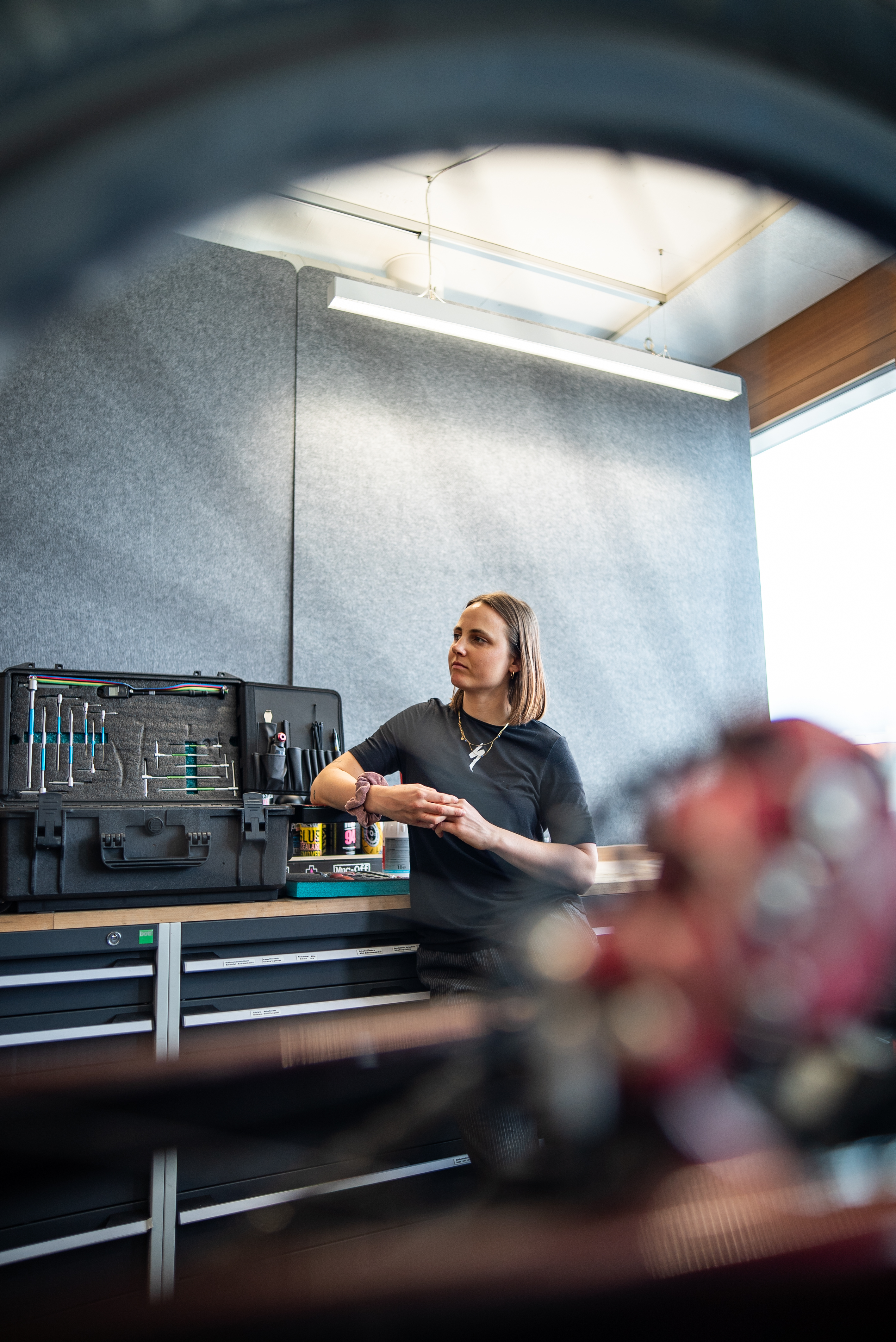 Sofia Wiedenroth is standing in a workshop in front of an open toolbox on a workbench. A bicycle part can be seen blurred in the foreground.